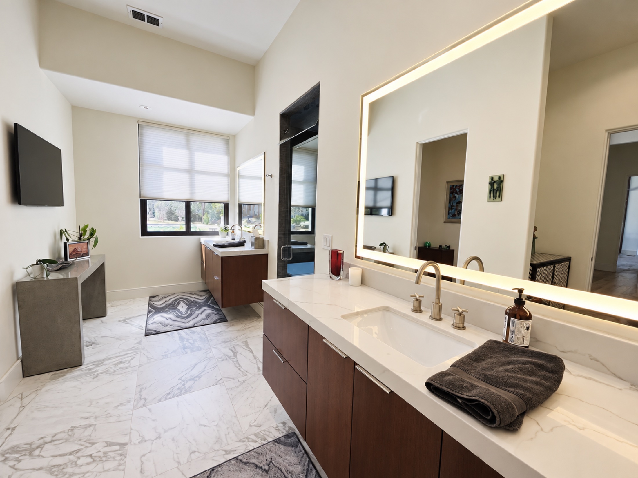 Spacious bathroom with walnut vanities and a large illuminated mirror
