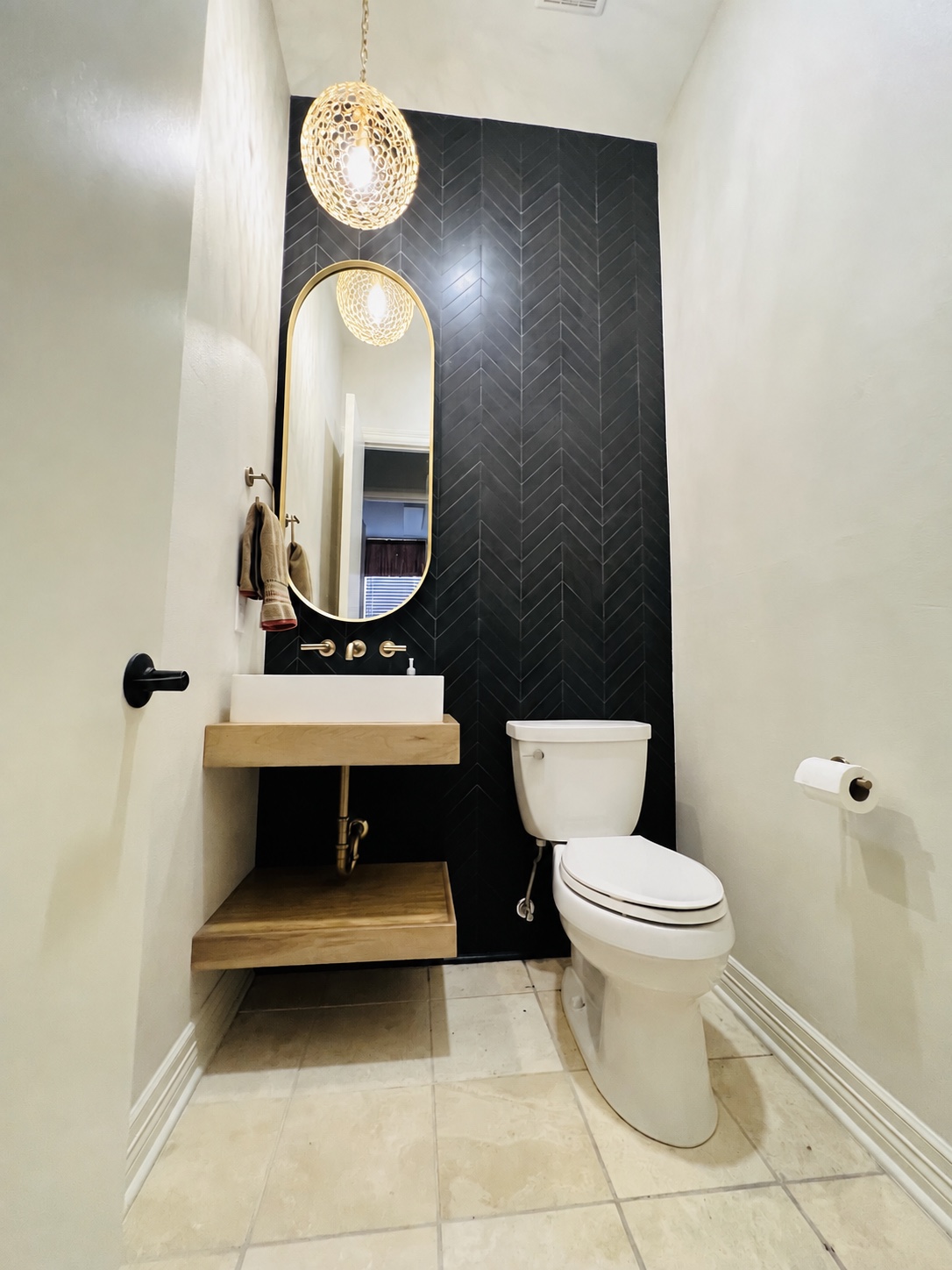 Digitally modified powder bathroom with a taller gold-framed arched mirror over a wood vanity and black chevron tile