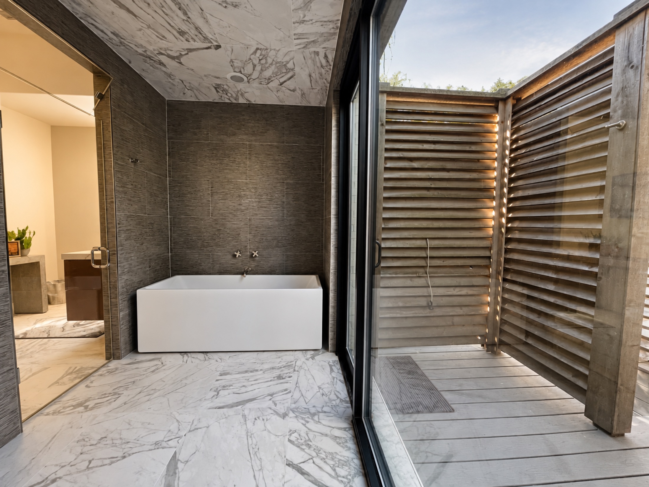 Dark stone bathtub alcove beside a private wood-screened courtyard