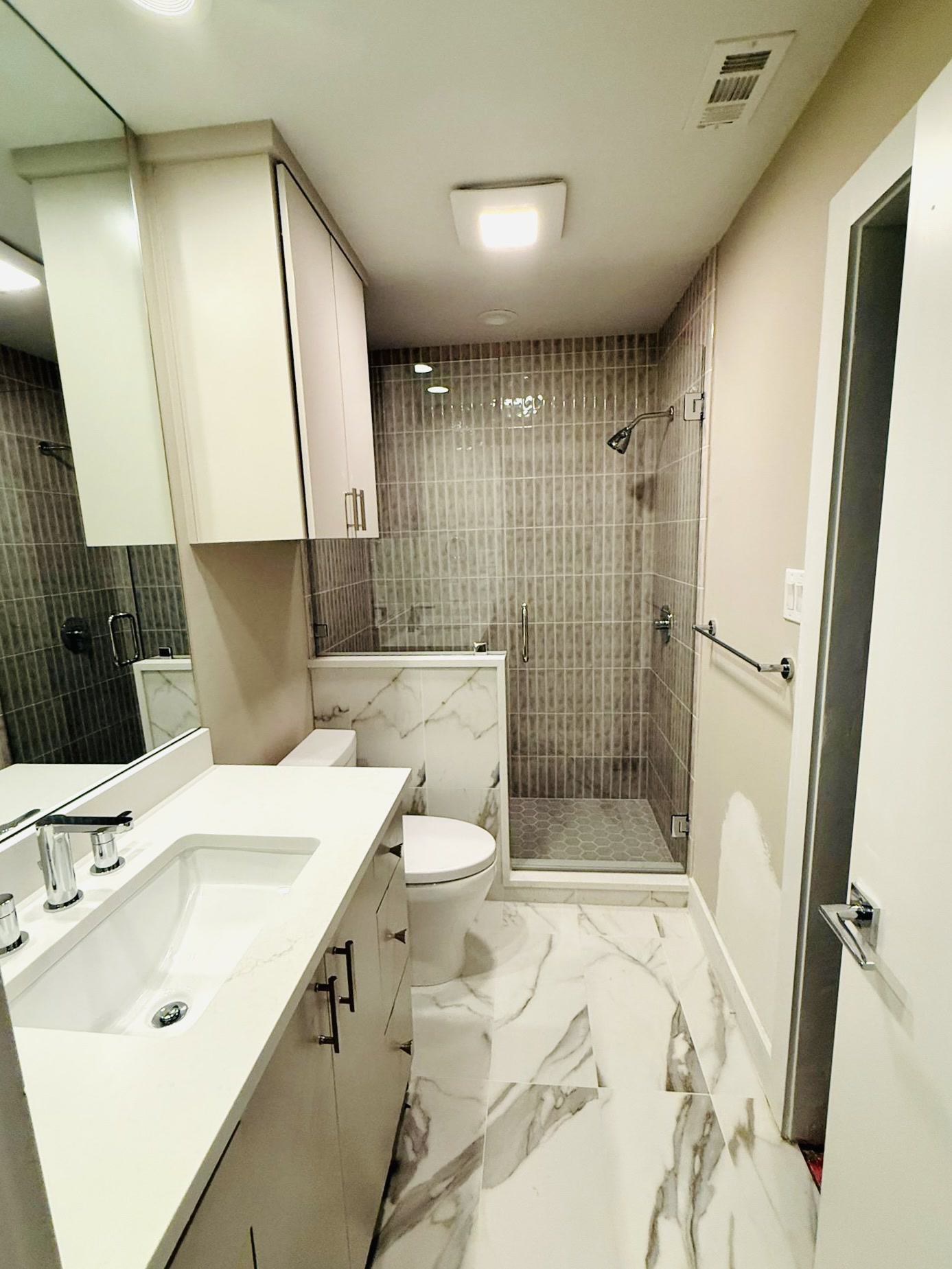 Contemporary bathroom with a white vanity, glass shower, gray vertical tile and marble-look floor