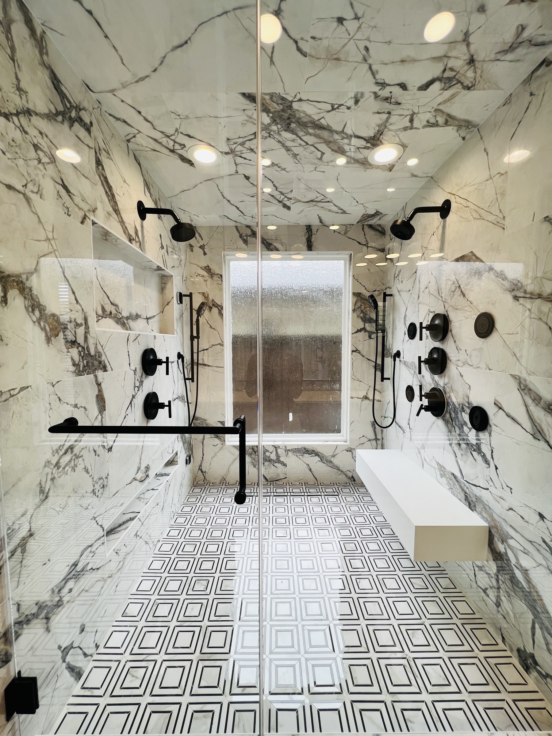 Marble-lined double shower with black fixtures, a built-in bench and geometric floor tile