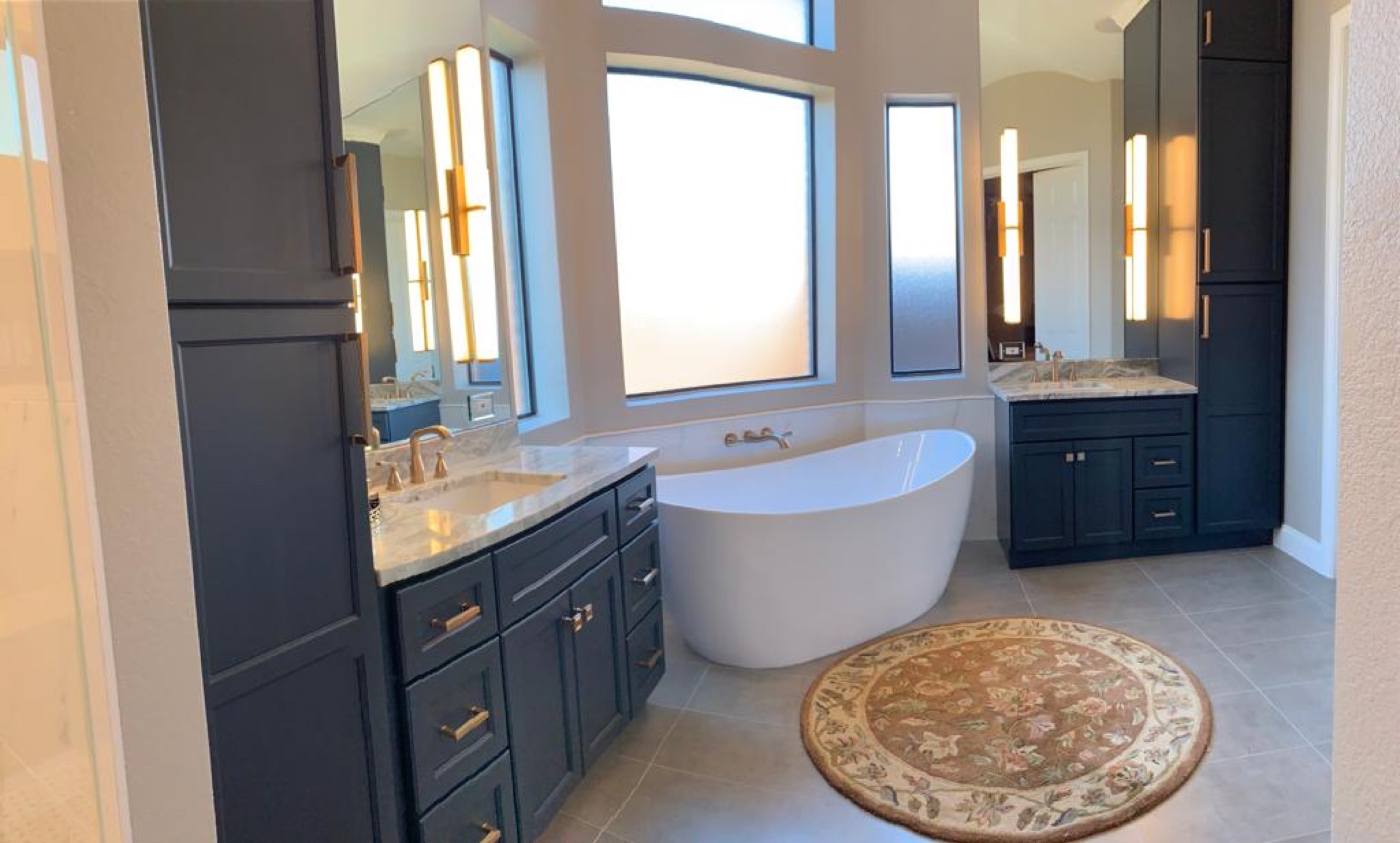 Primary bathroom with navy cabinets, freestanding white tub and tall windows