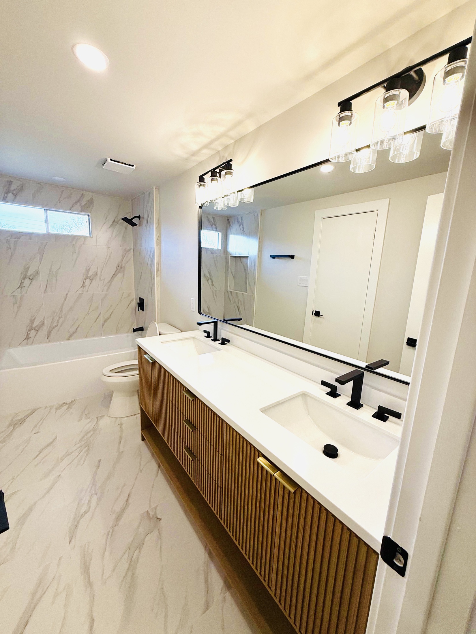 Marble bathroom with a walnut slat double vanity and black fixtures