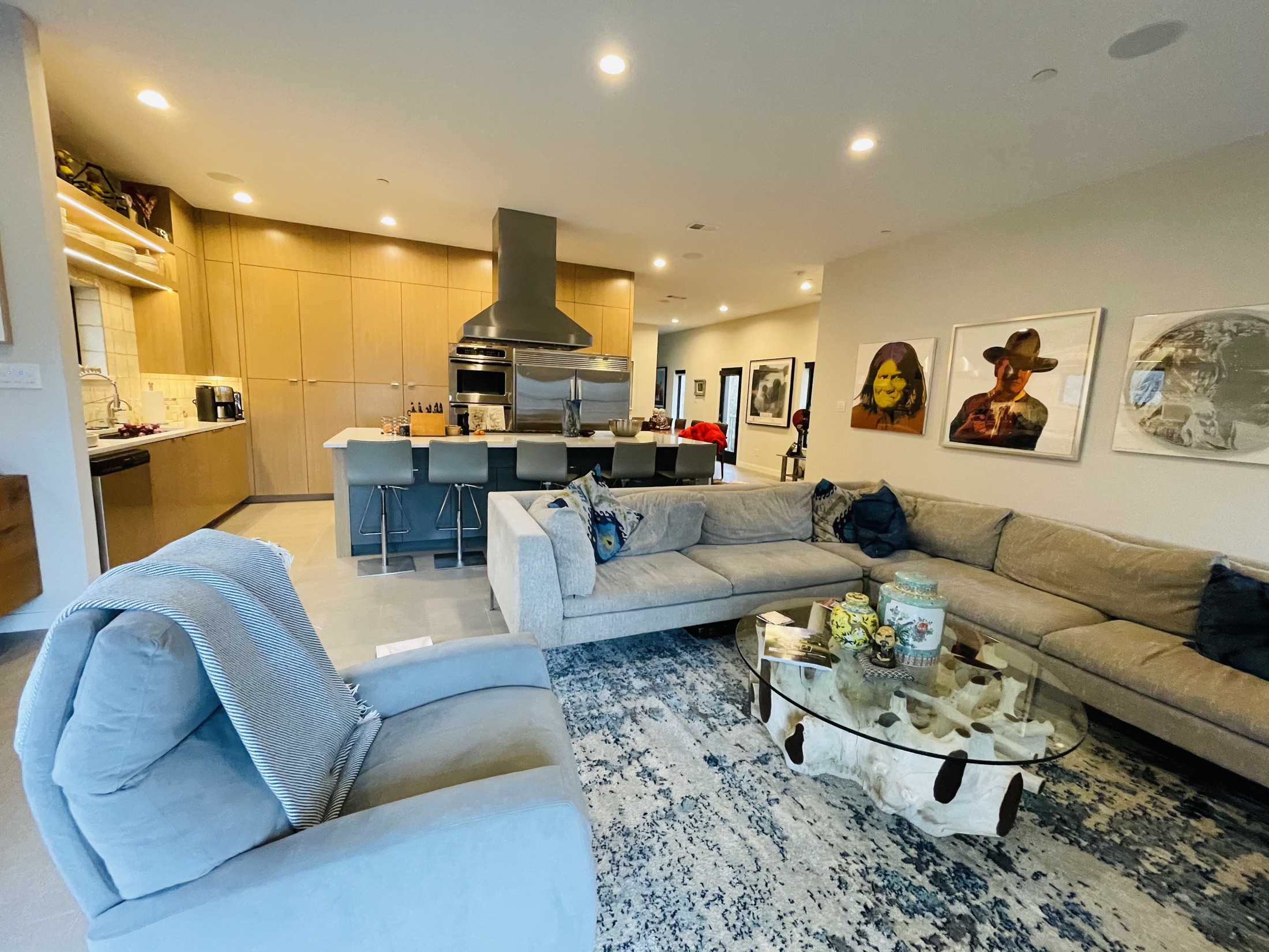 Living room with a sectional sofa, art collection and wood-paneled kitchen