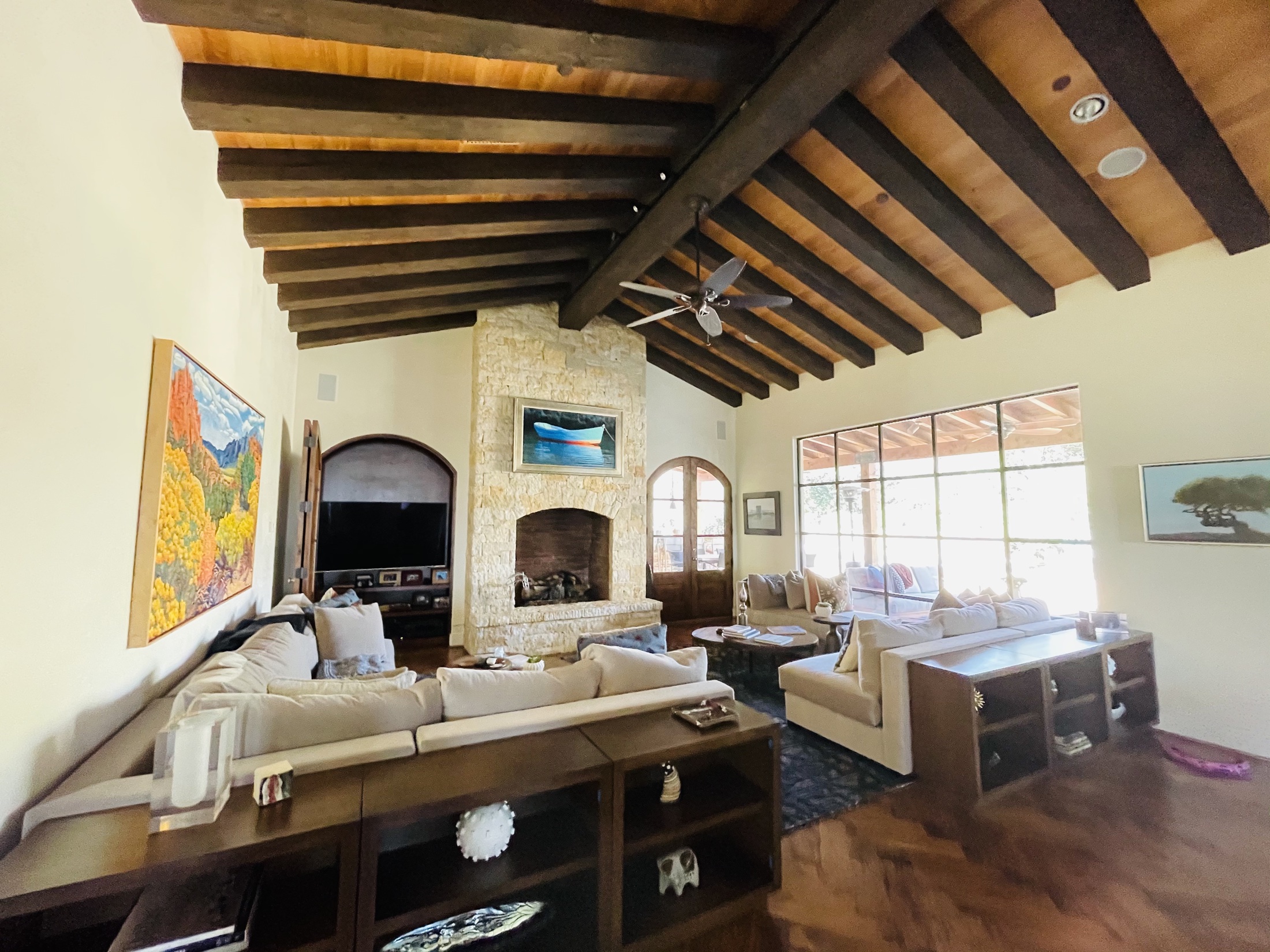 Living room with exposed wood beams, stone fireplace and large garden windows