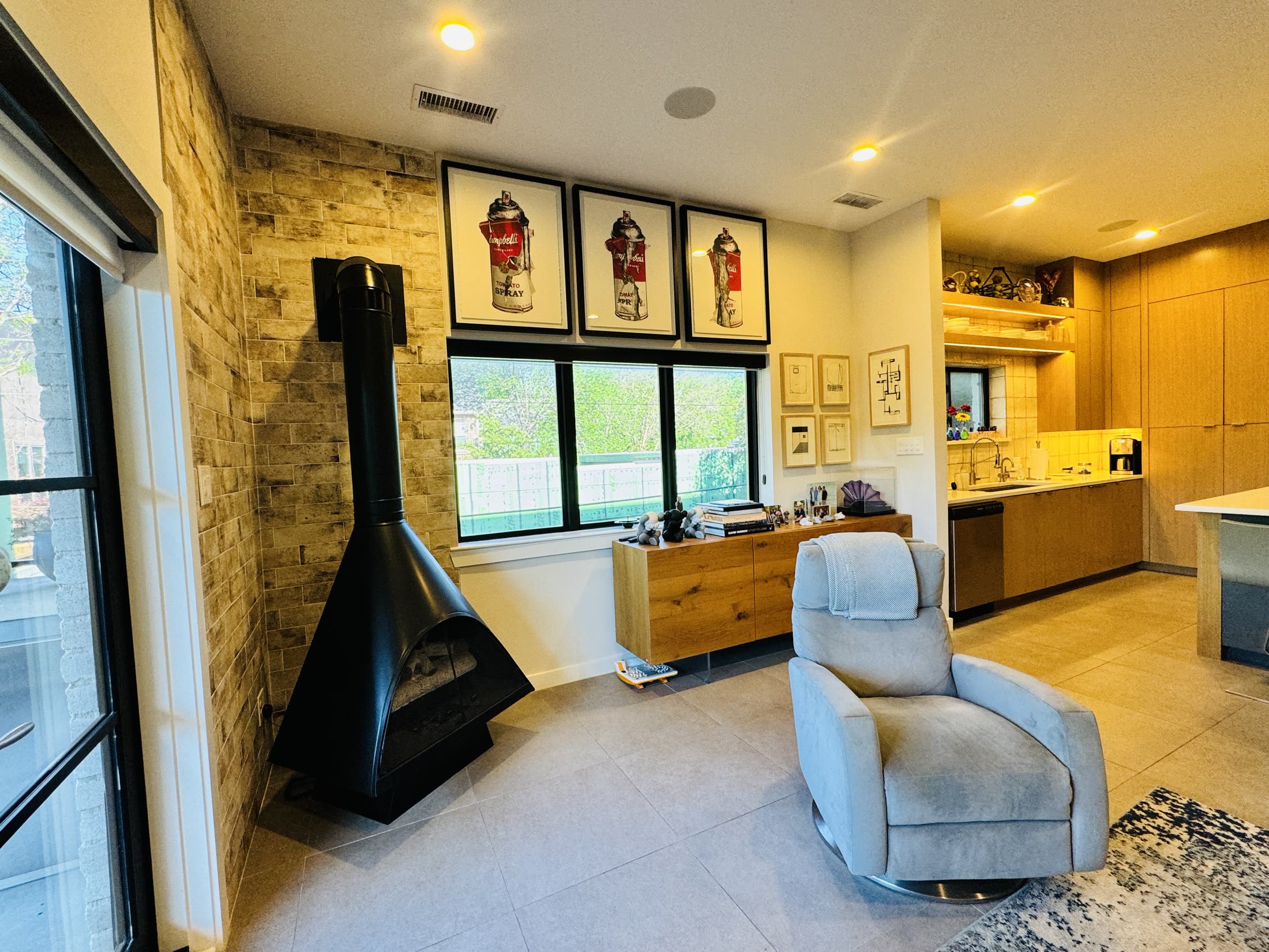 Modern lounge with a suspended black fireplace beside a wood-paneled kitchen
