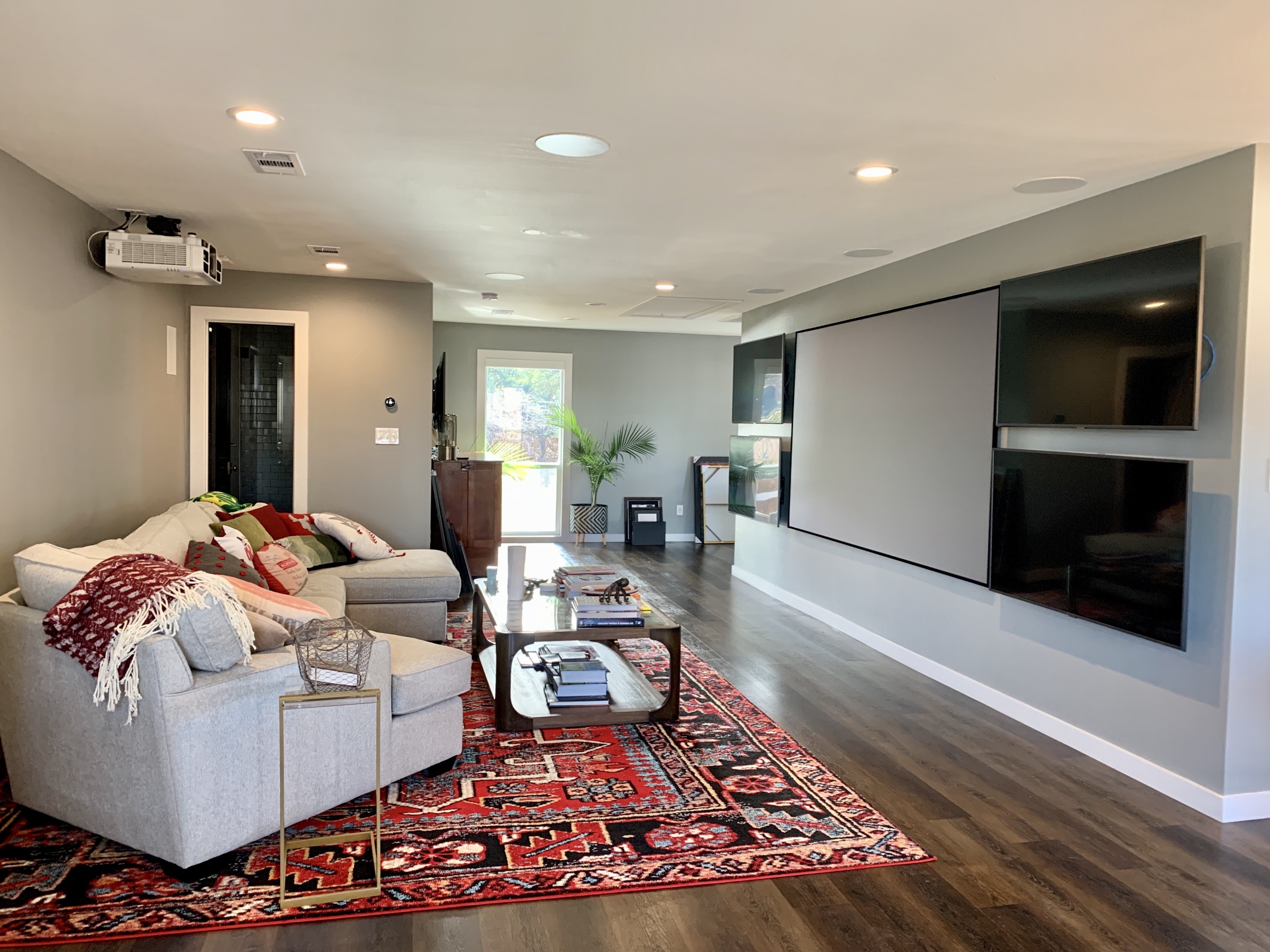 Media room with sectional seating, projection screen, wall-mounted displays and a red patterned rug