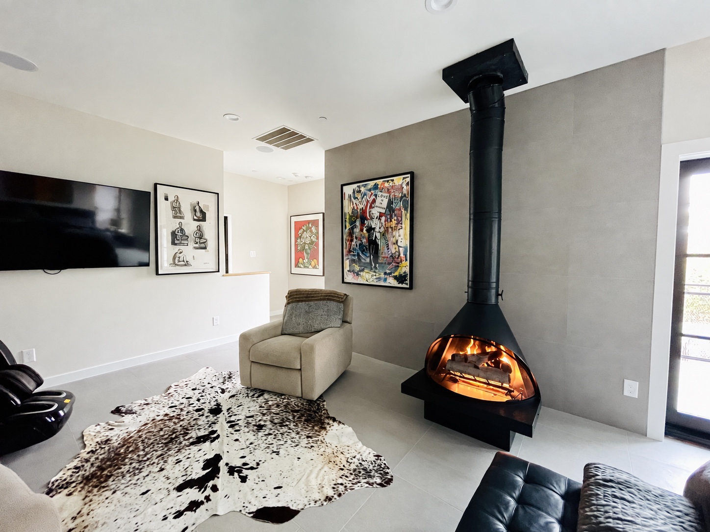 Art-filled living room with a suspended black fireplace, lounge seating and a cowhide rug