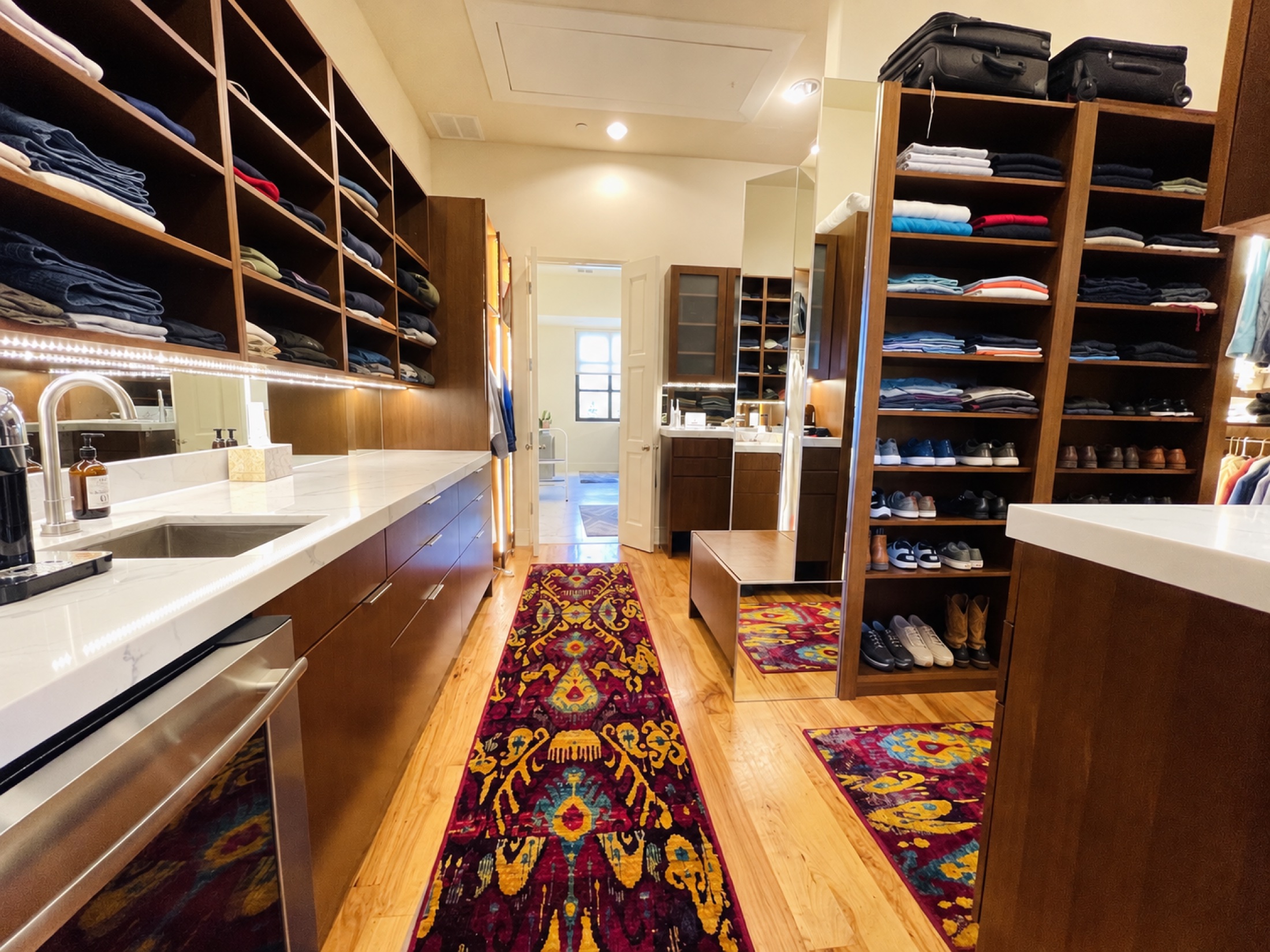 Walk-in closet with wood shelving, a vanity and a colorful carpet runner