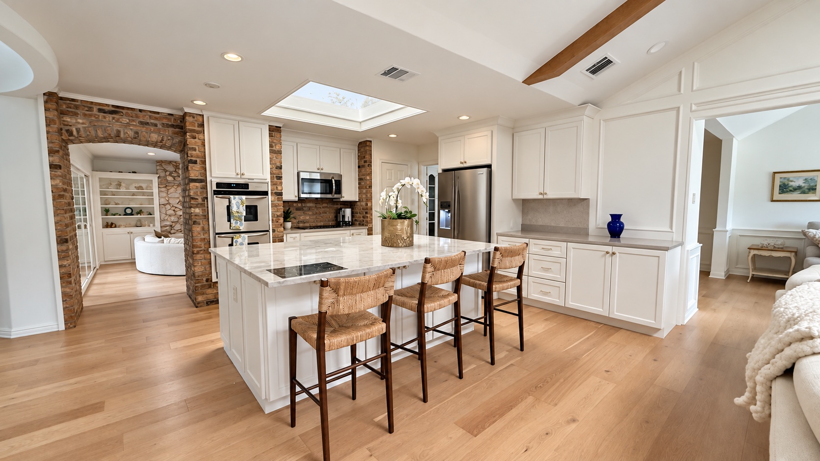Digitally refined white kitchen with brick arch, marble-look island, and three woven stools
