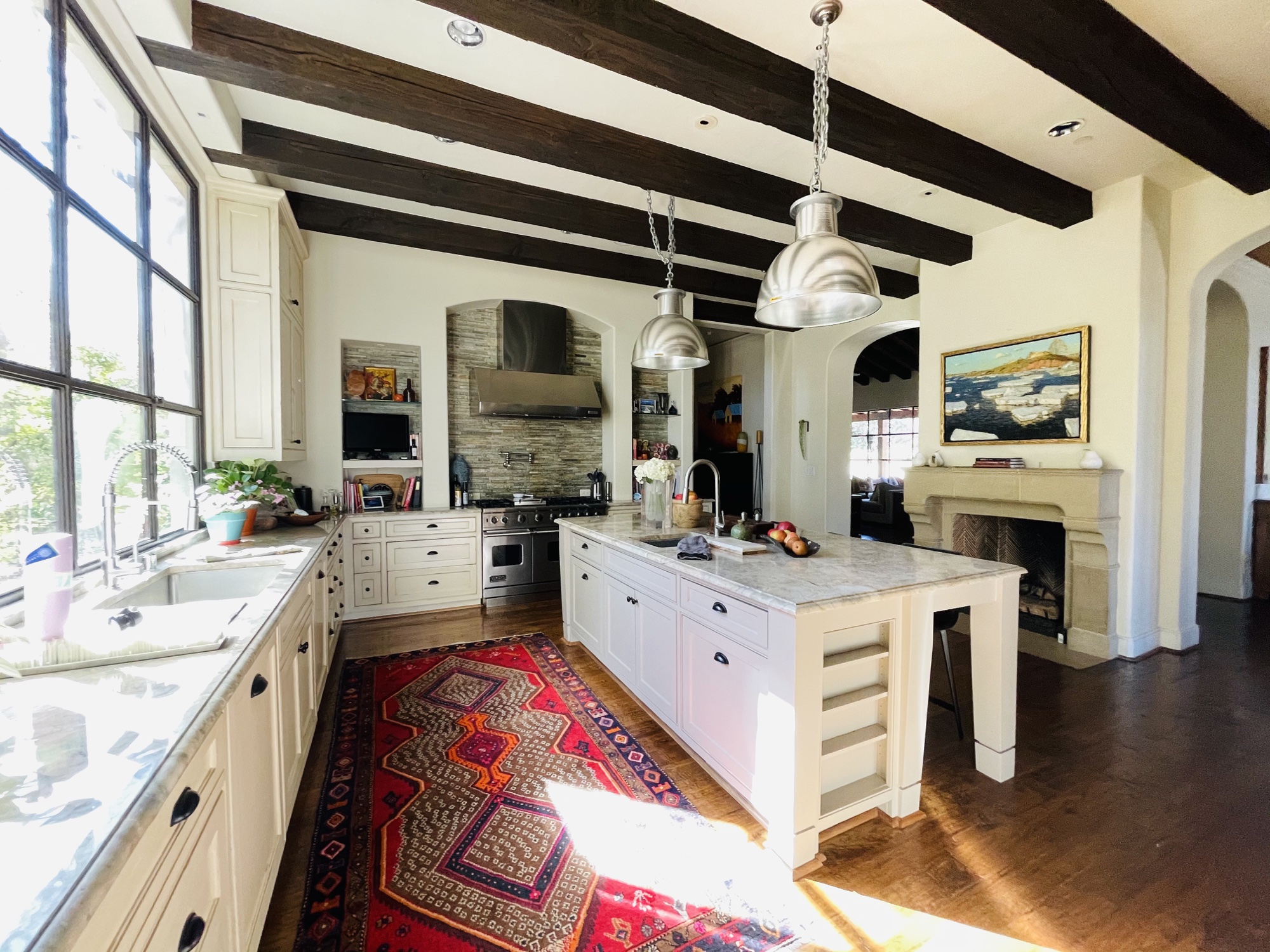 White kitchen with dark ceiling beams, large island and patterned red rug