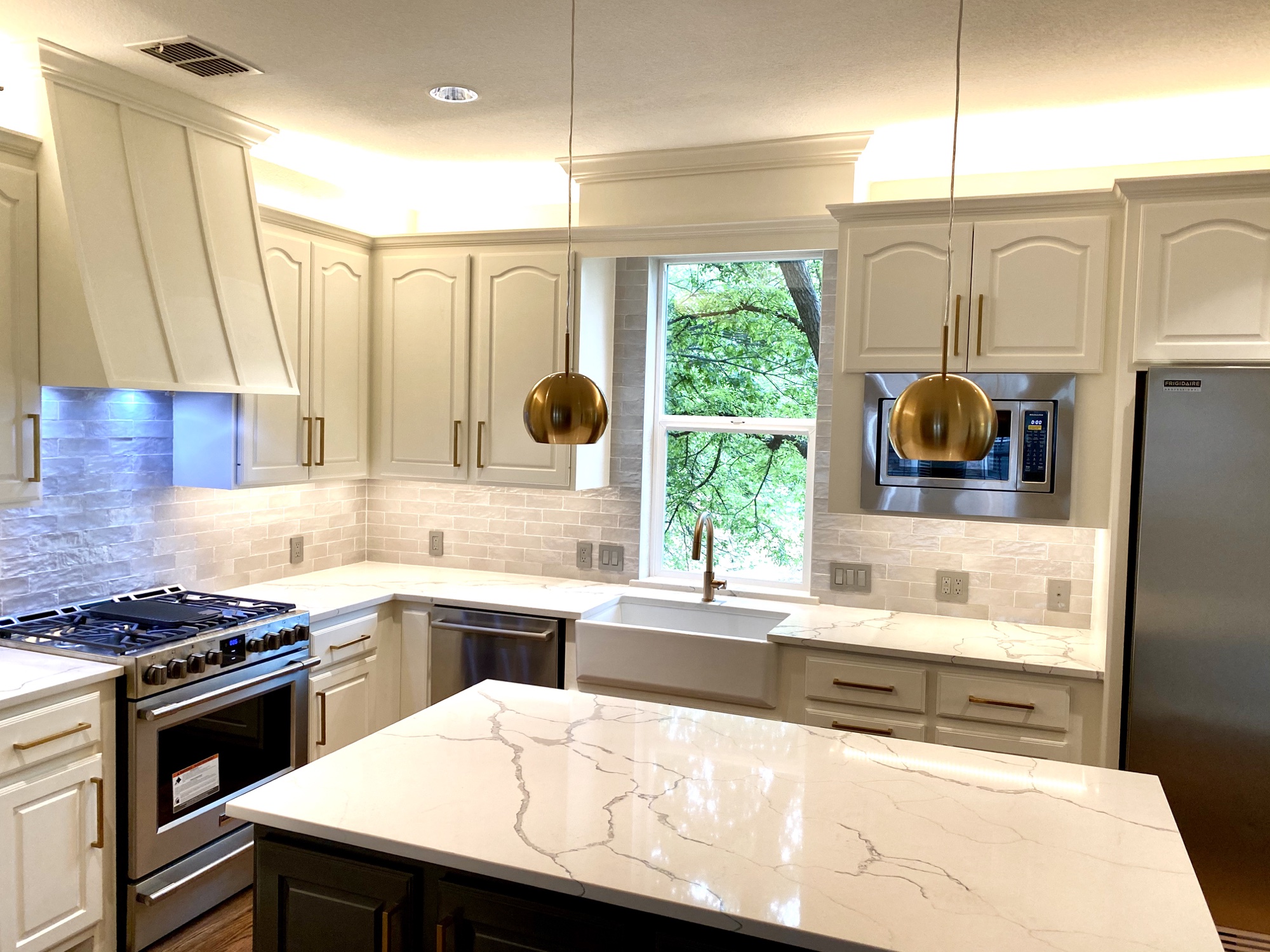 White kitchen with brass globe pendants and a window over the sink