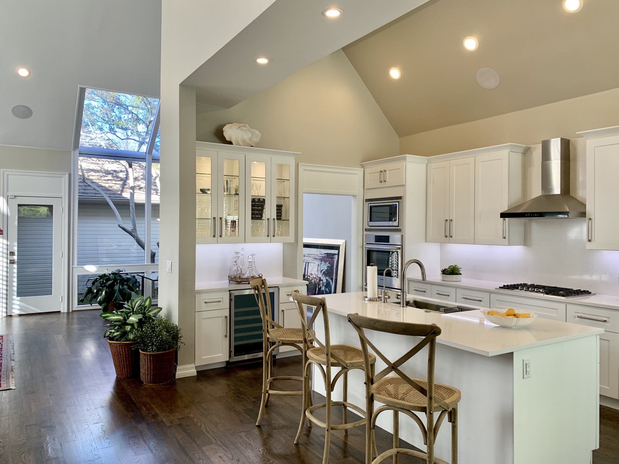 High-ceiling white kitchen with island seating and glass-front cabinetry
