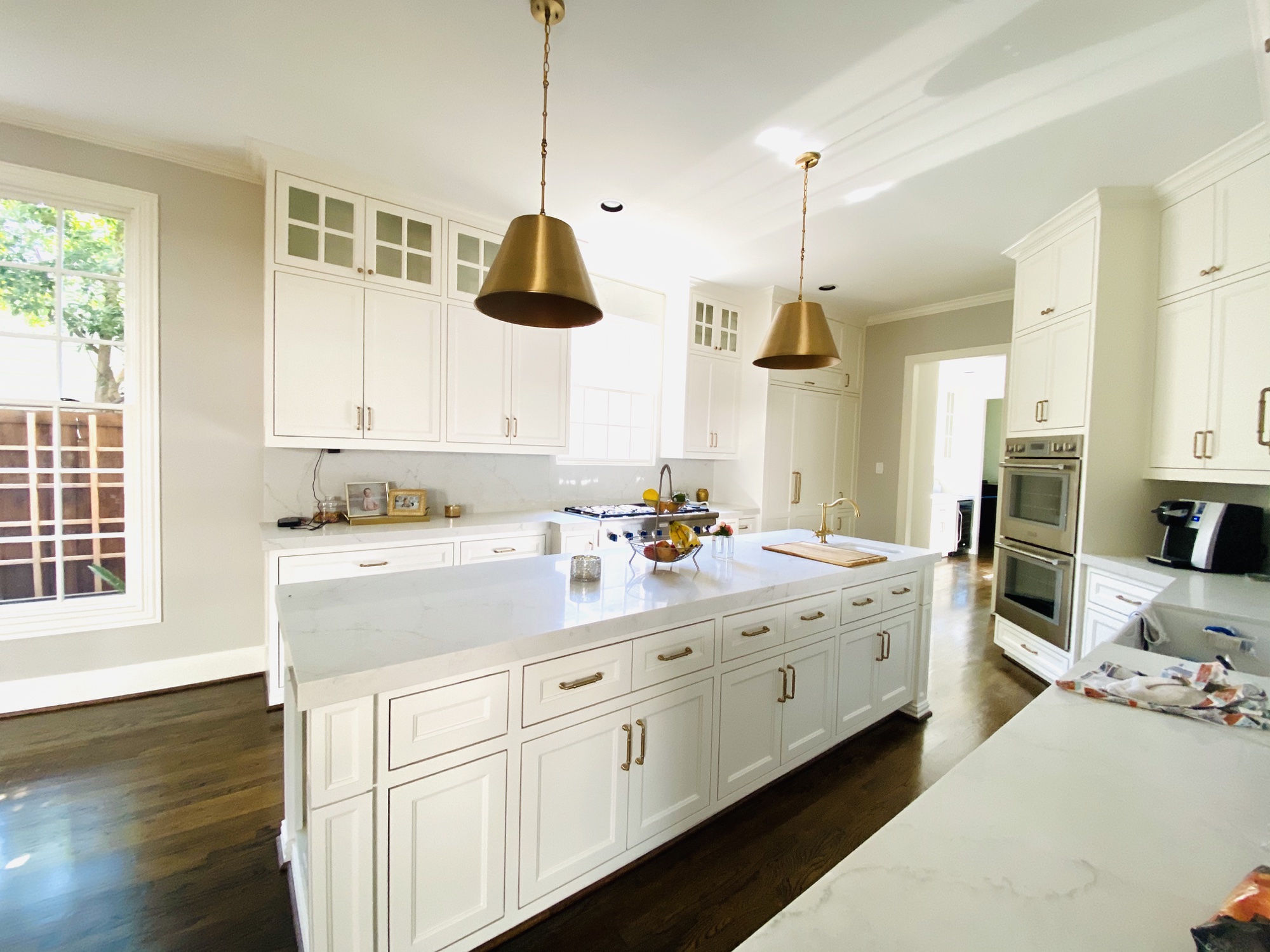 White kitchen with long marble island and two gold pendant lights