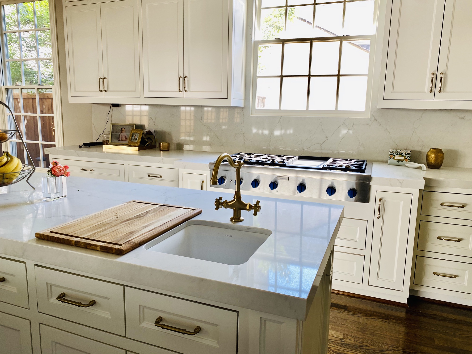 Close view of a white kitchen island with brass faucet, sink and range beyond