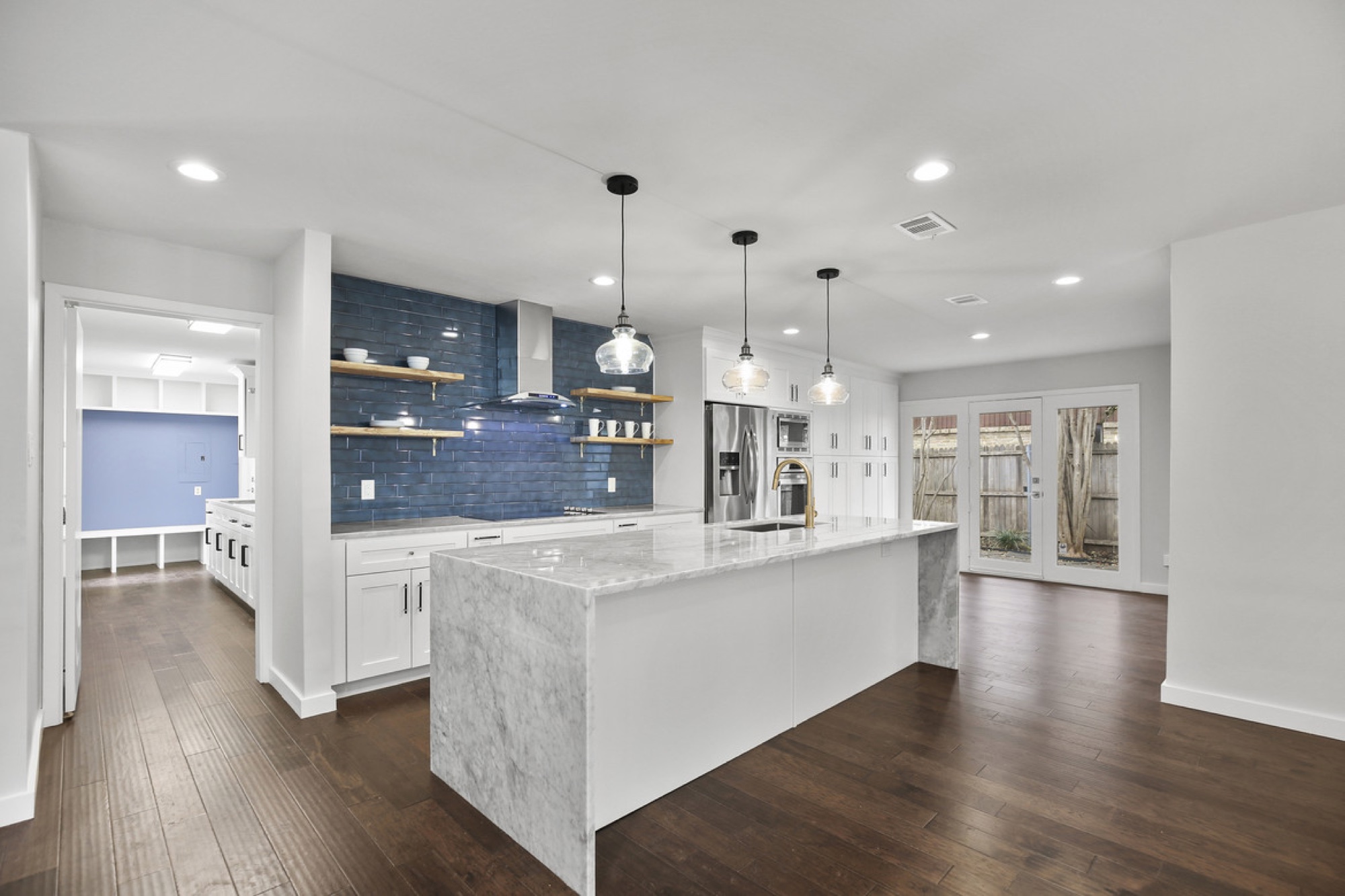 White kitchen with blue tile feature wall and marble waterfall island