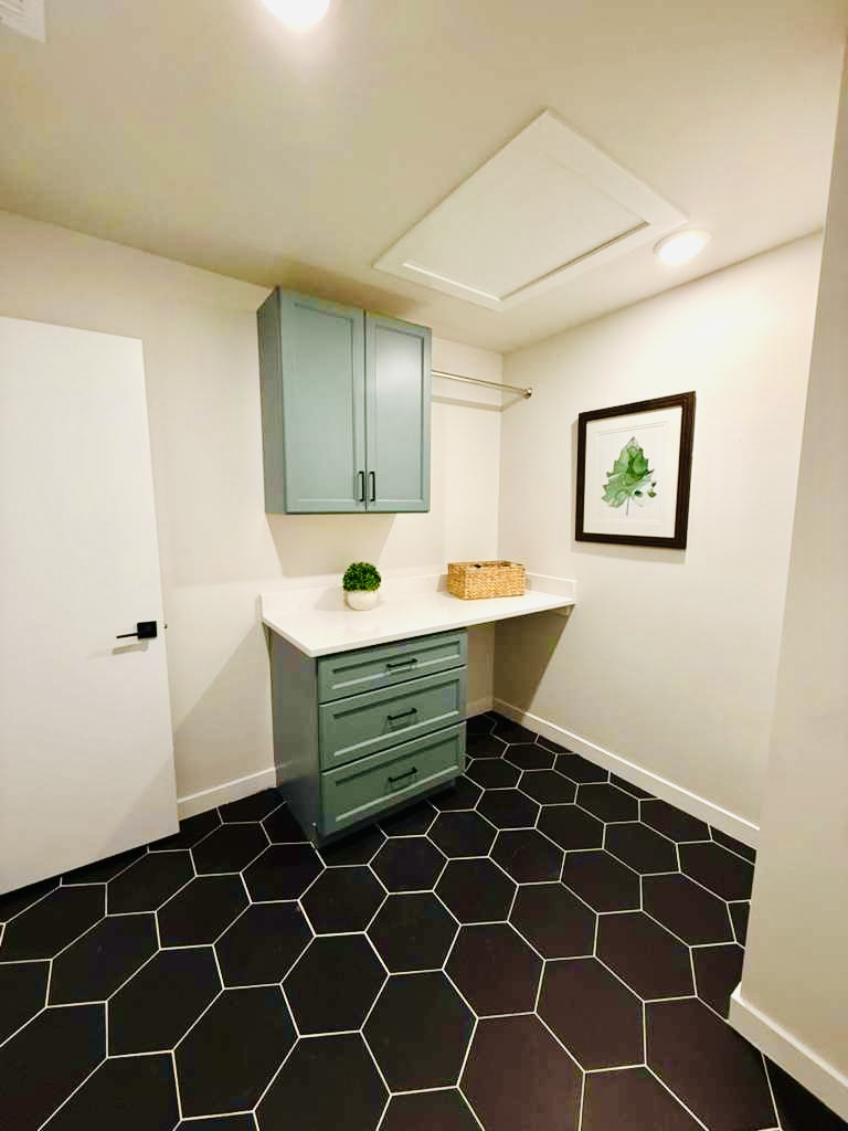 Laundry room with green cabinetry, a folding counter and black hexagonal floor tile