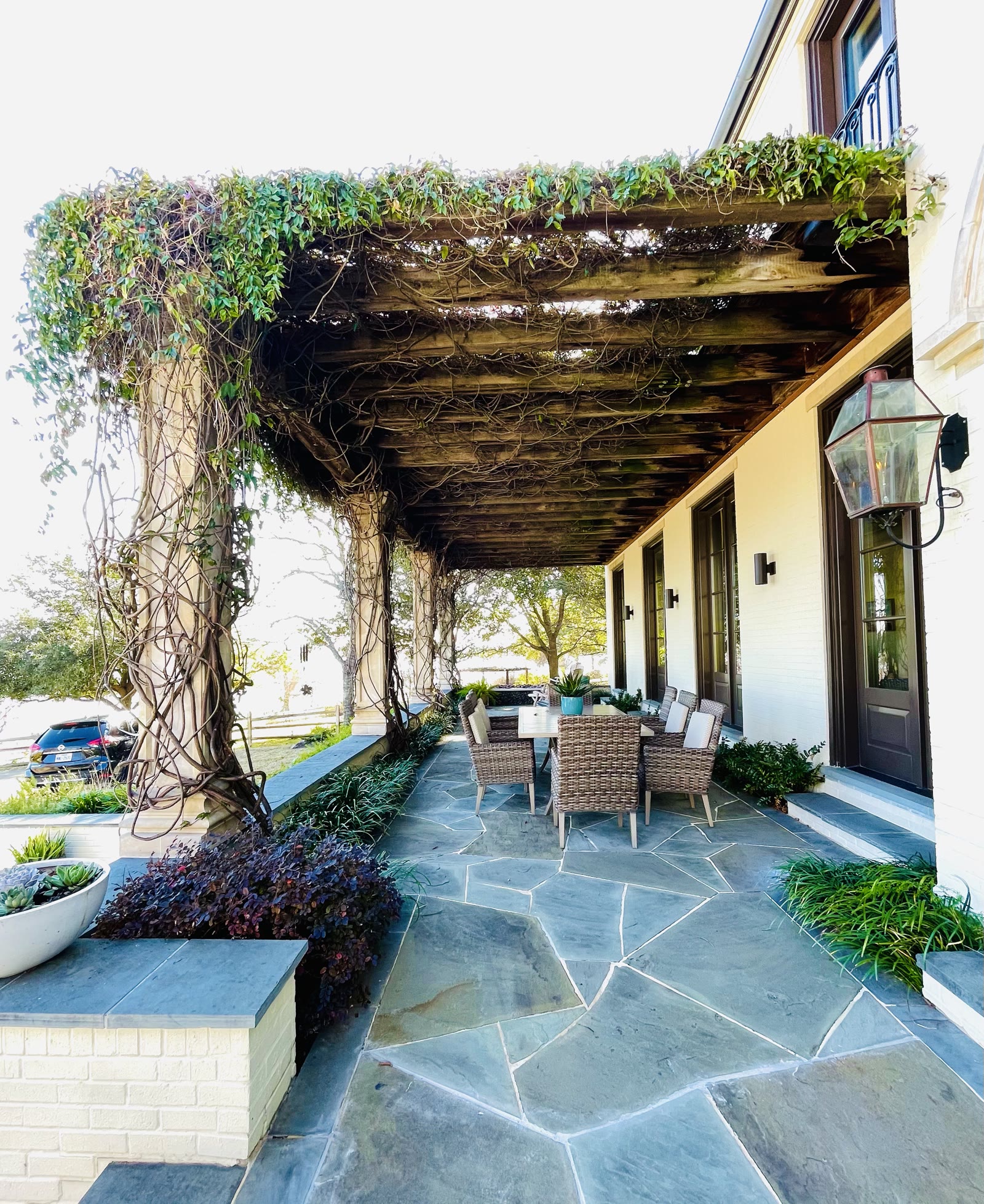 Vine-covered wood pergola over a blue stone patio with wicker dining furniture