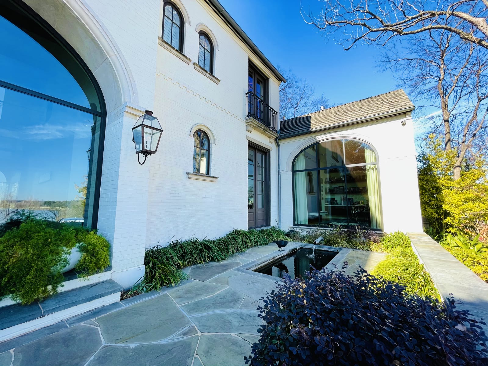 White brick home exterior with arched windows, blue stone terrace and reflecting water feature