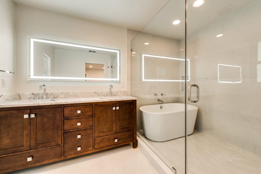 Modern bath with wood vanity, freestanding tub and illuminated mirrors