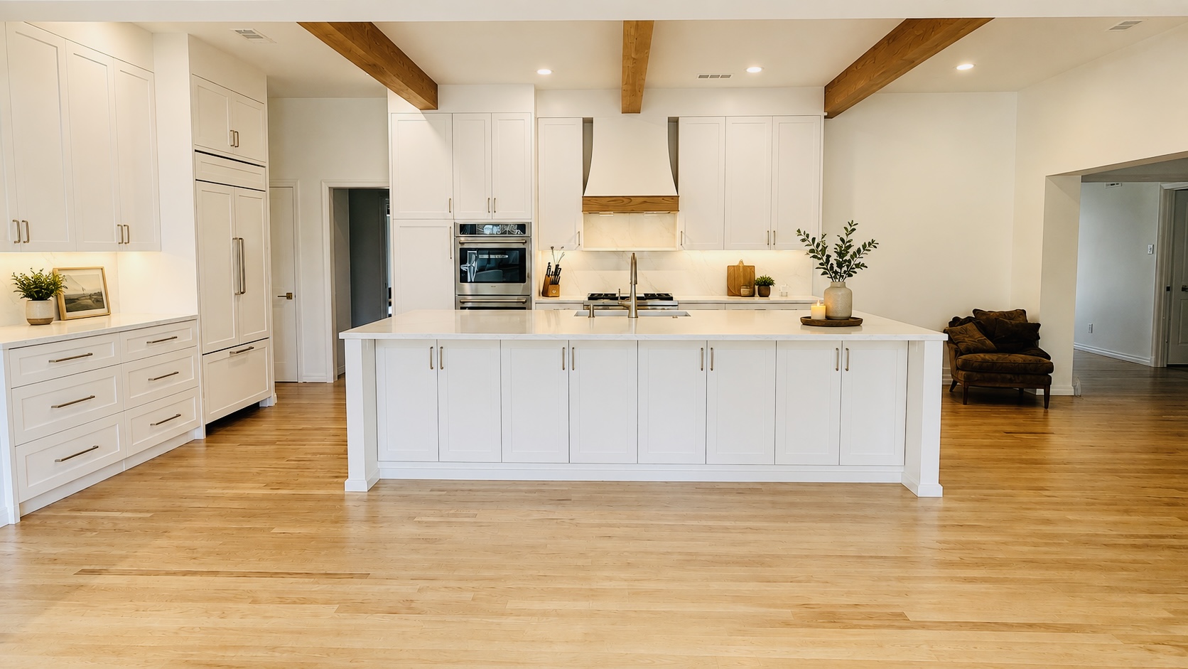 White kitchen with a large island, oak floors and exposed wood beams