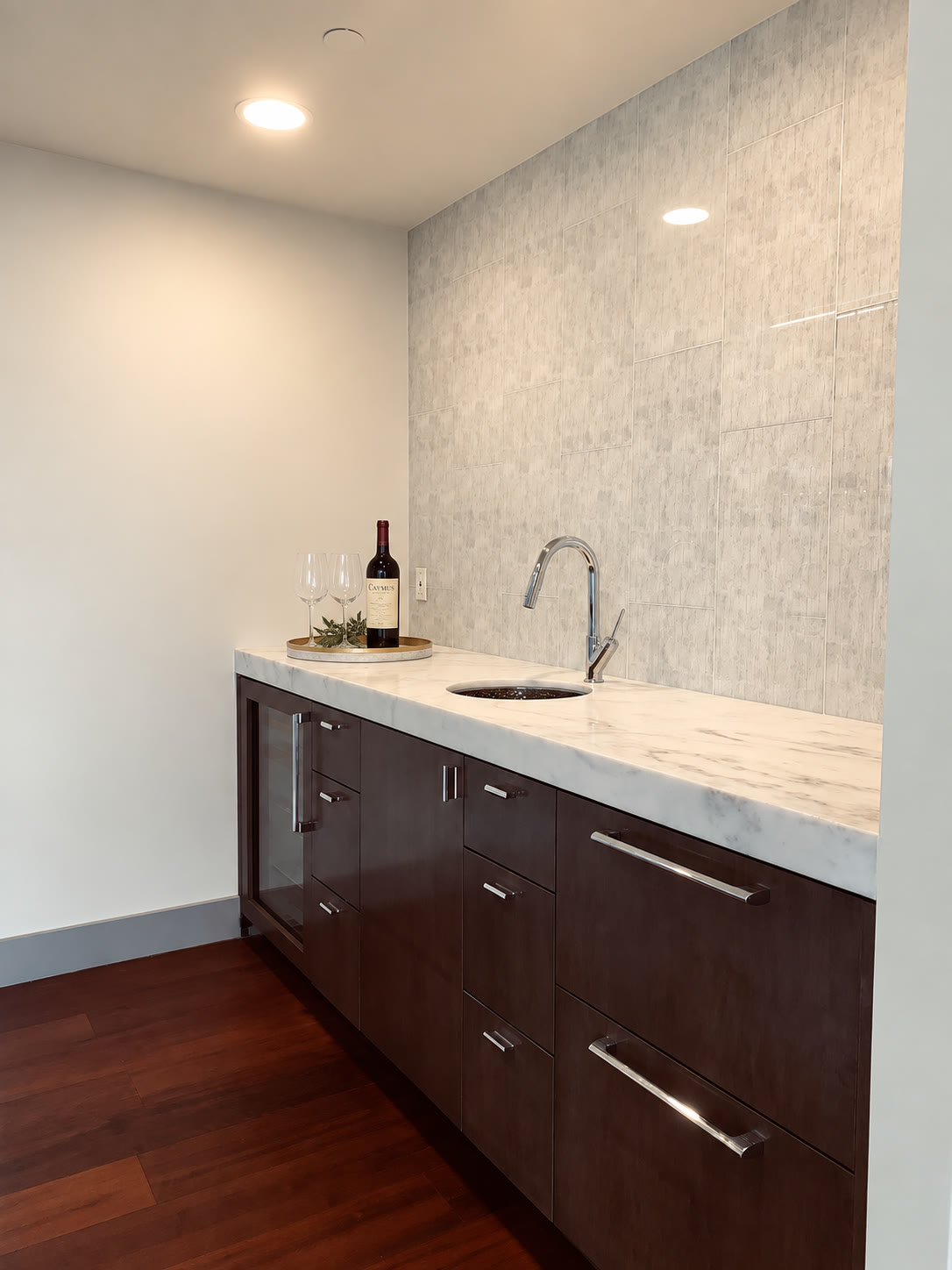 Dark wood wet bar with marble counter, blue tile wall and digitally staged wine service