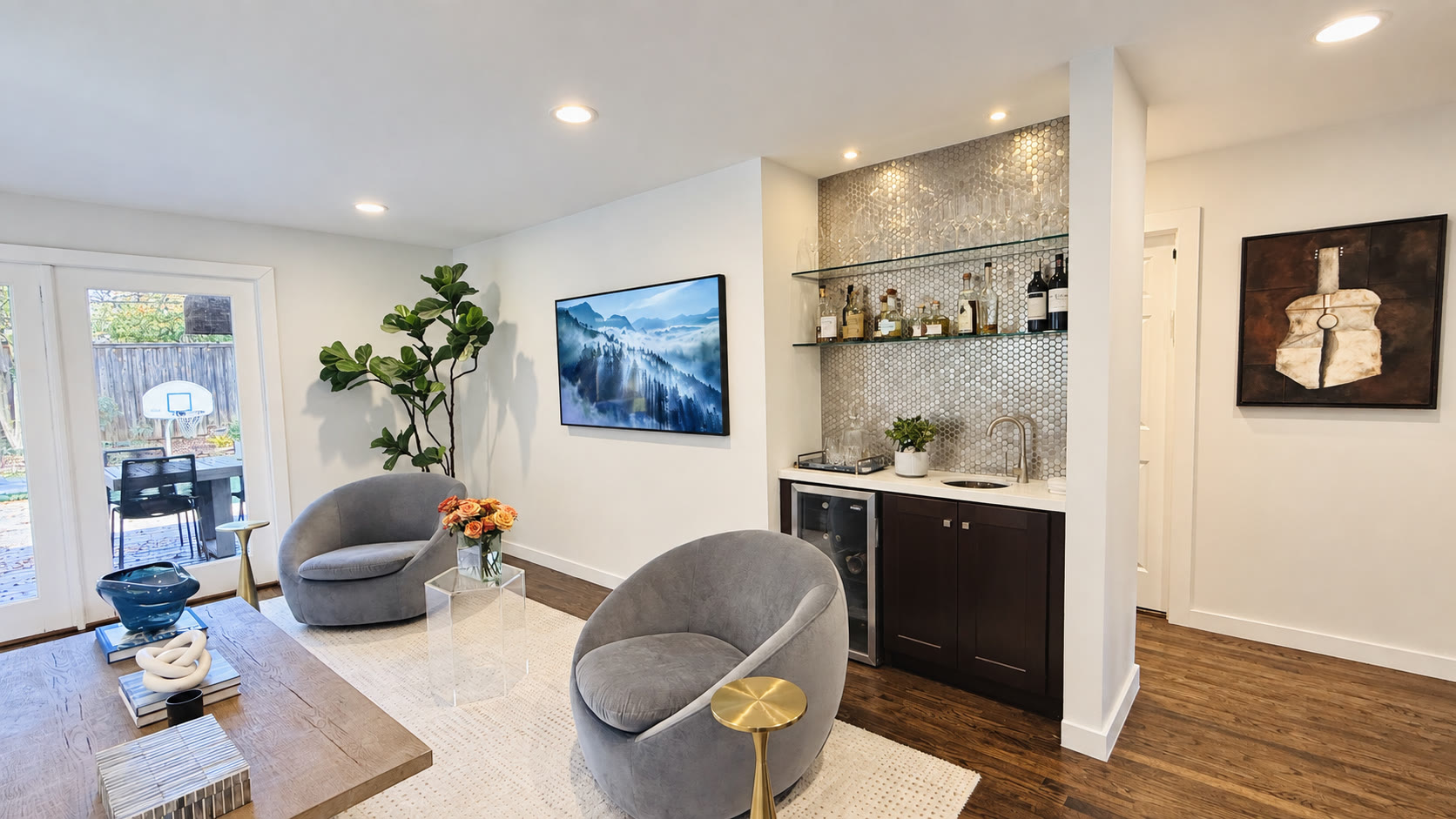 Lounge seating beside a home bar with glass shelves and reflective tile